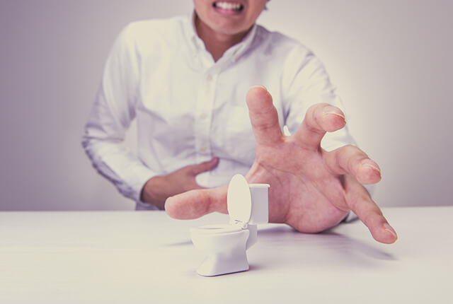 お腹を右手で押さえる男性とトイレの模型のイメージ
